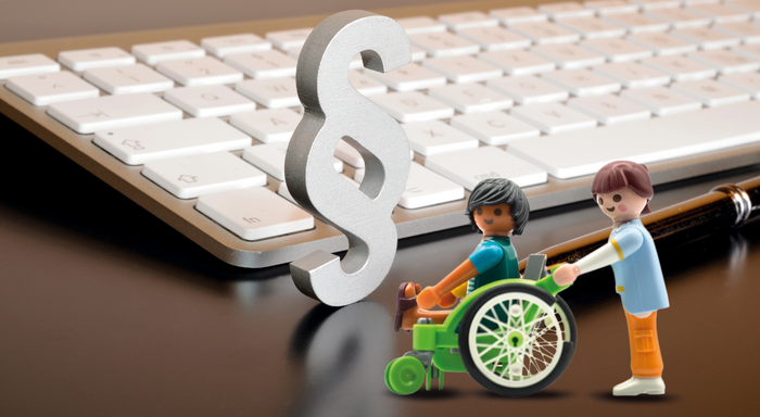 Paragrafenzeichen vor Tastatur mit Playmobilmännchen in Rollstuhl