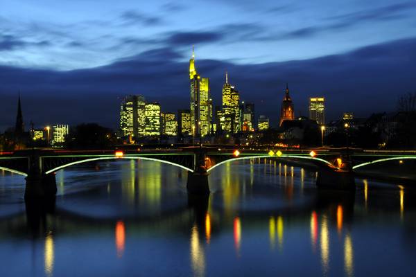 Bild der Skyline von Frankfurt in der Nacht. Man sieht die beleuchteten Hochhäuser sowie den dunklen Main im Vordergrund.