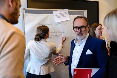 Das Foto zeigt Teilnehmende der ersten Workshop-Runde im Austausch vor einem Plakat.