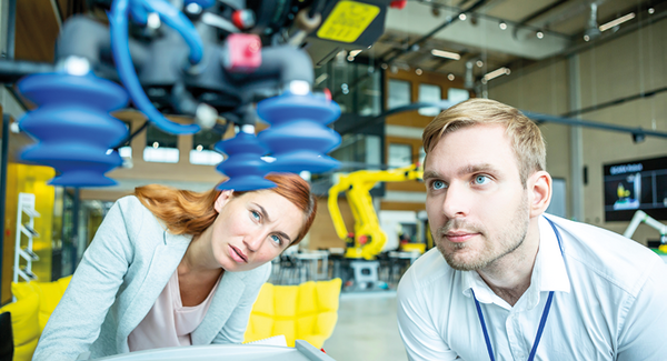 Abbildung von einer Frau und einem Mann, die zusammen die Arbeit eines Roboterarms beobachten